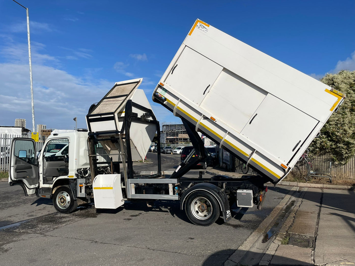 White garbage truck with its rear lift gate open on a street.