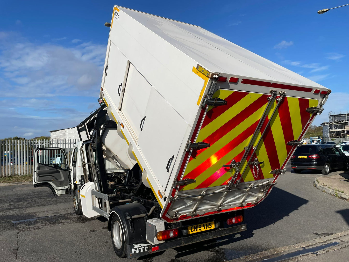 White tipper truck with red and yellow warning stripes on a road.