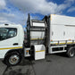White garbage truck with open rear door on a road under a blue sky with clouds.