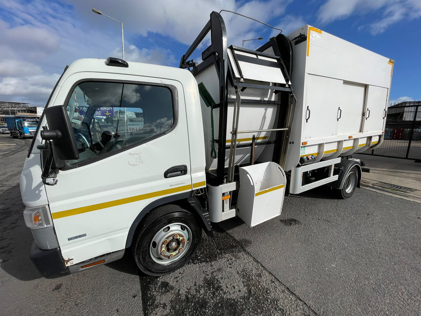 White garbage truck with open rear compartment on a road