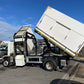 White garbage truck with its rear lift gate open on a street.